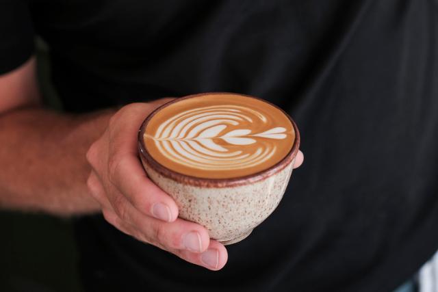 Kaffekop med cappuccino med flot latteart i toppen holdes af en hånd