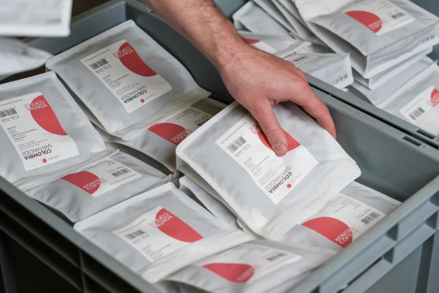 Hånd tager en hvid kaffepose fra kasse fuld af hvide kaffeposer