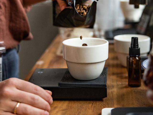 Kaffeboenner haltes ned i en hvid skål, der står paa en kaffevægt