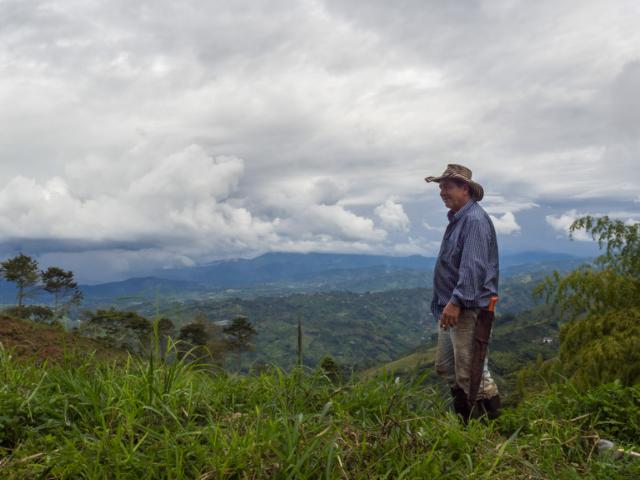 Mand med cowboyhat, smøg i hånden og machete i bæltet står med udsigt til bjerglandskab