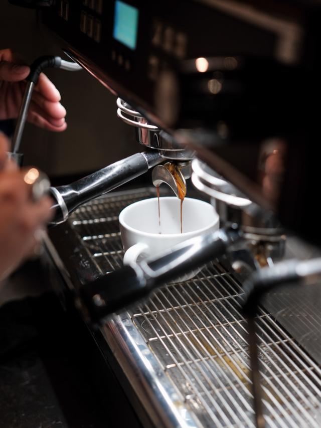 Espressobrygning på espressomaskine espresso løber ned i hvid kaffekop med hank