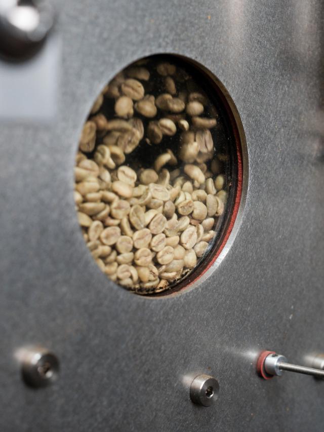 grønne kaffebønner der ristes og kan ses igennem rundt vindue