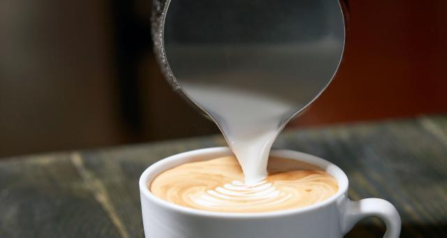 Closeup af mælk der hældes fra en steamkande ned i en kaffekop